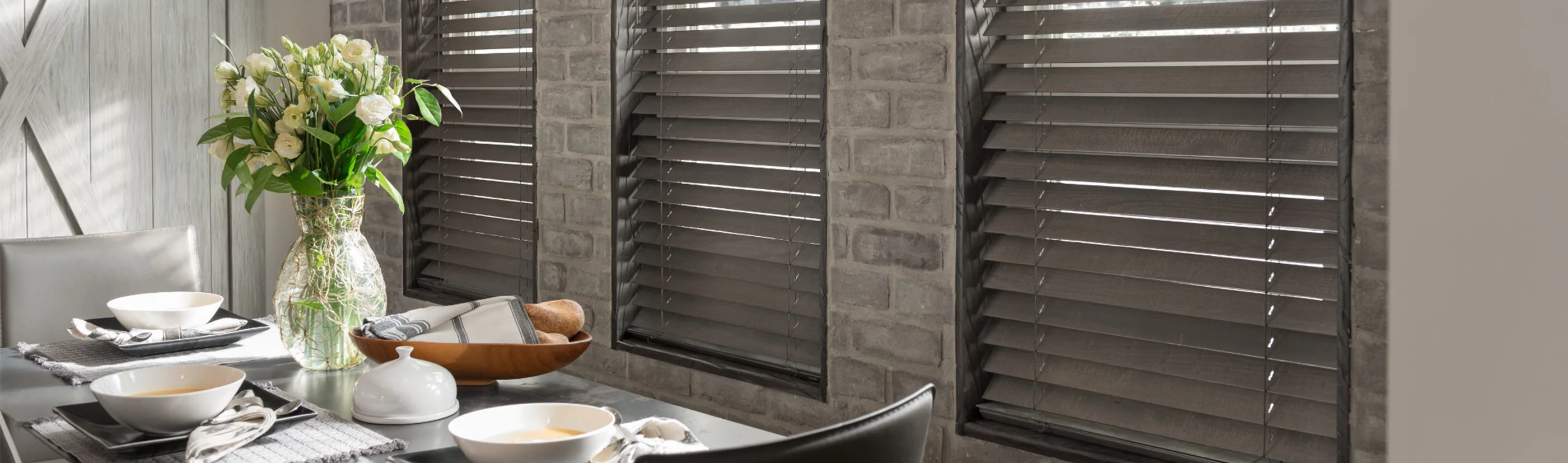 dark gray wood blinds in three tall windows next to a dining table with decor