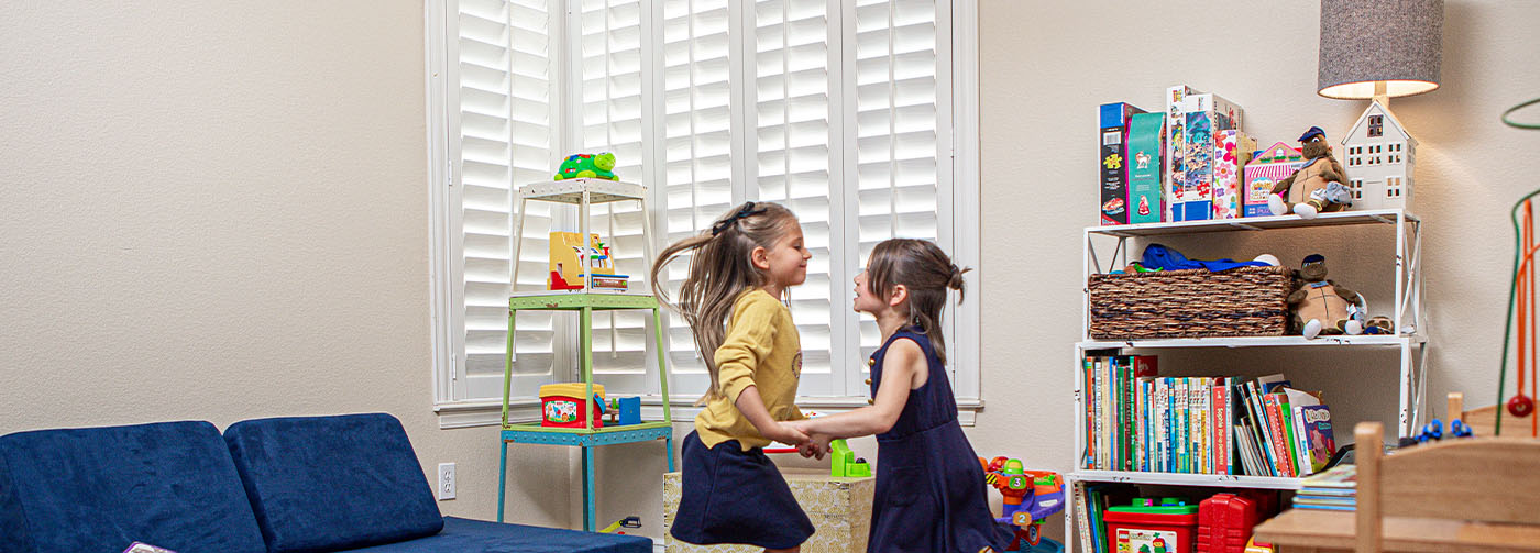 two girls playing next to white polywood shutter windows