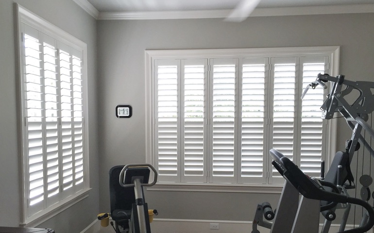 Draft-blocking window treatments are vital in spaces with windows on more than one wall. Atlanta exercise room with shuttered windows.