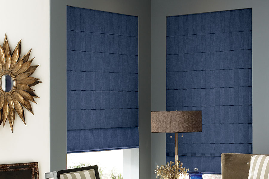 Available in a range of styles and colors, Roman shades are suitable for nearly any space. This distinctive blue option blends perfectly in a modern living room. Navy blue Roman shades in a corner of a modernly decorated living room.