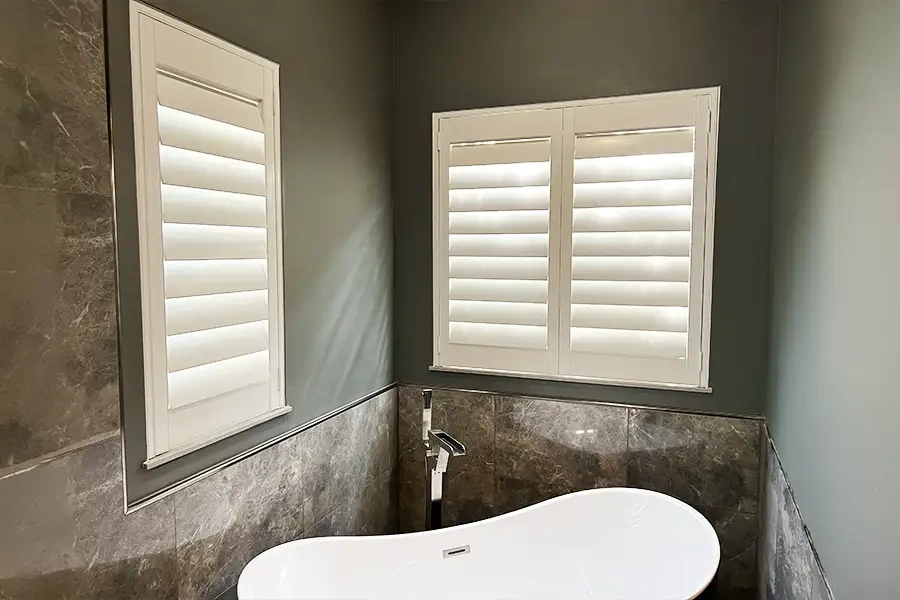 Customizable and moisture-resistant, Polywood shutters are the best choice for small bathroom windows. White Polywood shutters above a tub in a bathroom